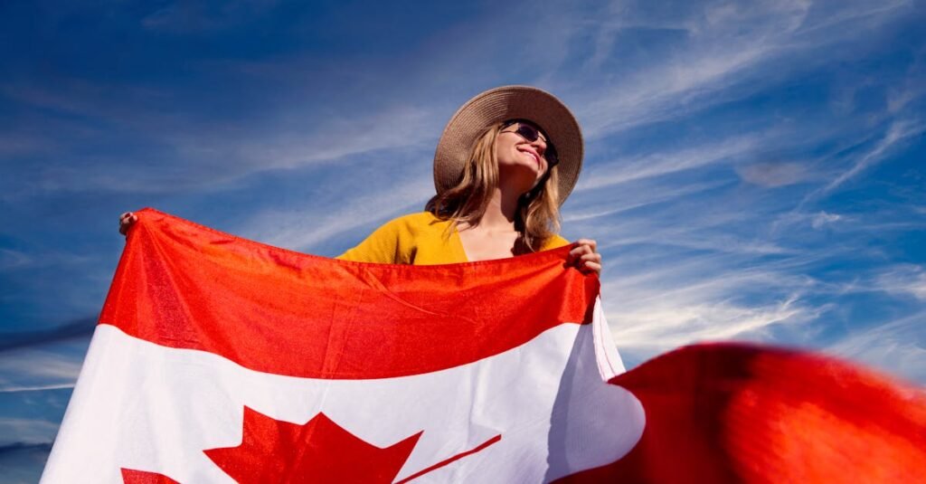 A joyful woman holding the Canadian flag under a clear blue sky, symbolizing national pride.